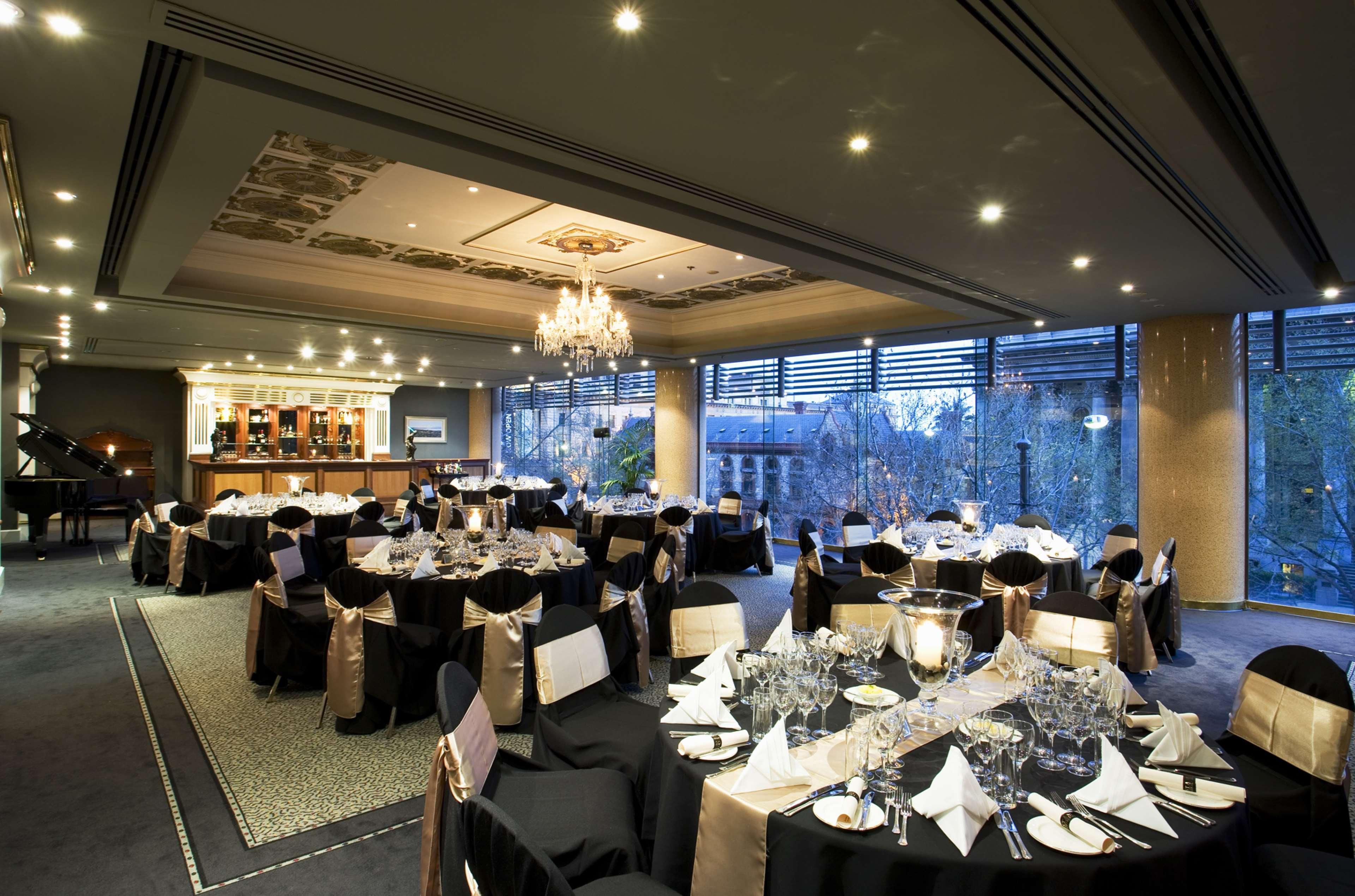 Stamford Plaza Adelaide Hotel Bagian luar foto The photo shows an elegant banquet hall or restaurant setting. There are several round tables covered with black tablecloths and adorned with gold accents. Each table is set with fine dining utensils, glassware, and neatly folded napkins. In the back