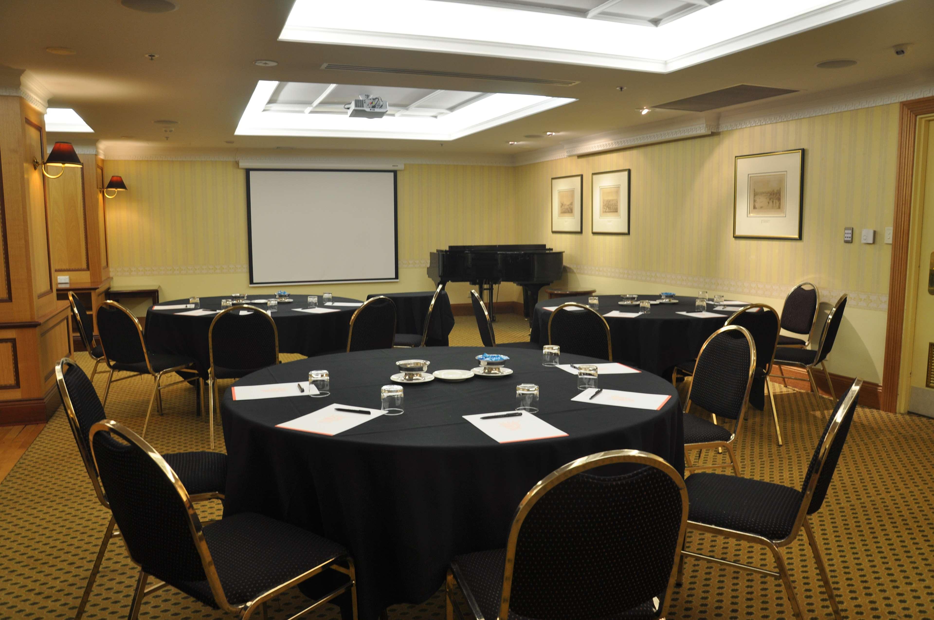Stamford Plaza Adelaide Hotel Bagian luar foto The photo shows a conference room set up for a meeting or presentation. There are several round tables covered with black tablecloths, each surrounded by black upholstered chairs. On the tables, there are notepads and glasses of water, indicating tha