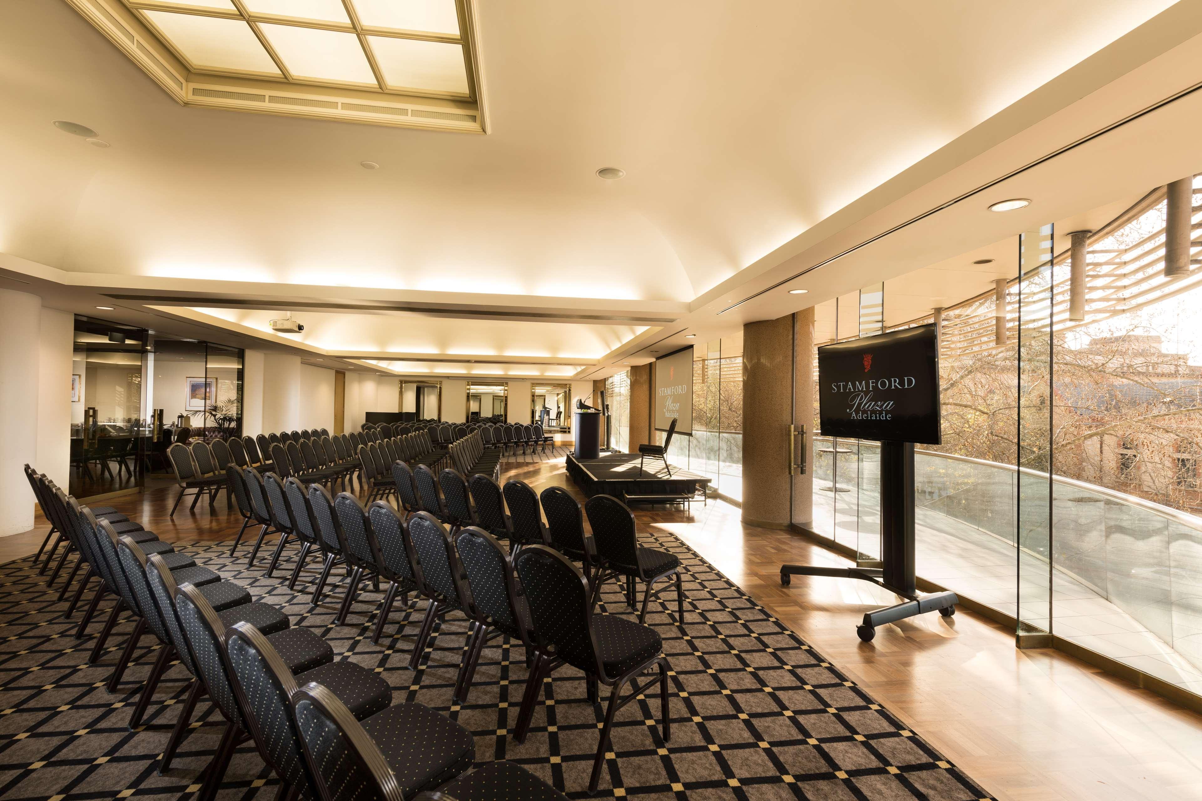 Stamford Plaza Adelaide Hotel Bagian luar foto The photo shows a large, elegantly designed event space or meeting room. There are rows of black chairs set up facing a presentation area. The flooring features a patterned carpet, and large windows allow natural light to enter the room. On one side,