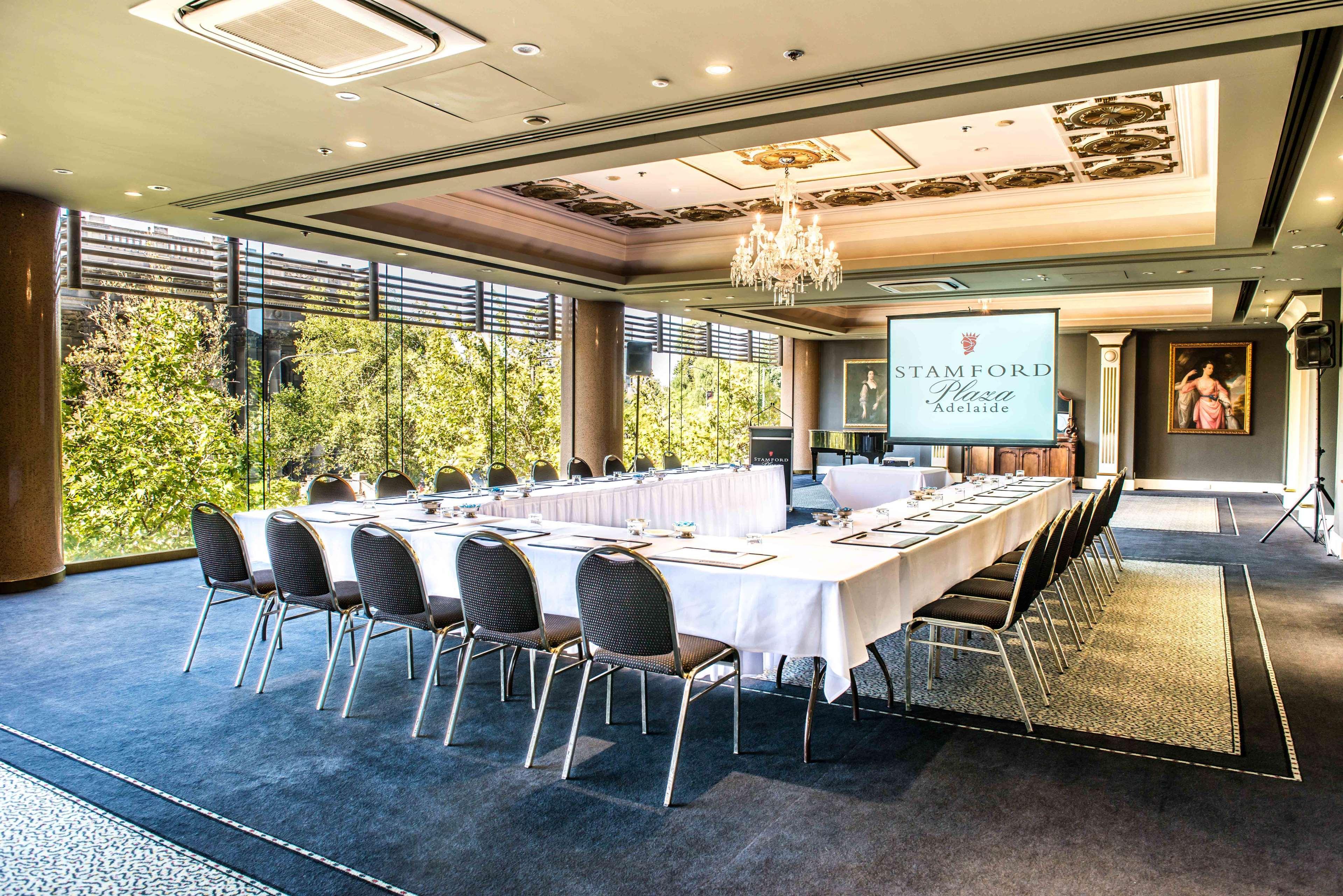 Stamford Plaza Adelaide Hotel Bagian luar foto The photo shows a stylish conference room set up for a meeting or event. There is a long rectangular table covered with a white tablecloth, surrounded by black chairs. A large screen displays the name "Stamford" along with a logo. The room features l
