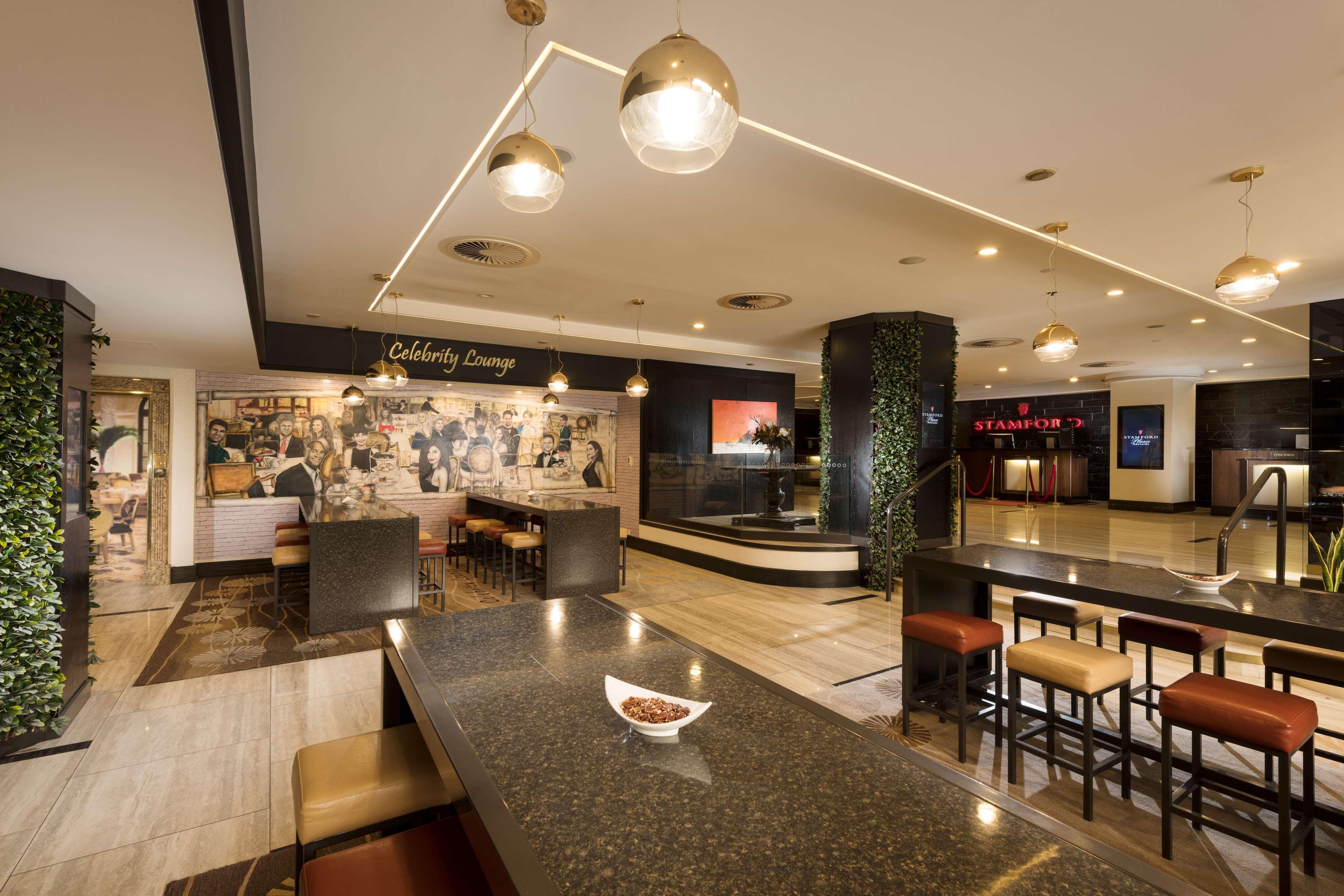 Stamford Plaza Adelaide Hotel Bagian luar foto The photo shows a modern and stylish interior of a lounge or restaurant area. Prominent features include a long dark countertop with bar stools, and several pendant lights hanging from the ceiling. In the background, there is a mural or artwork that 