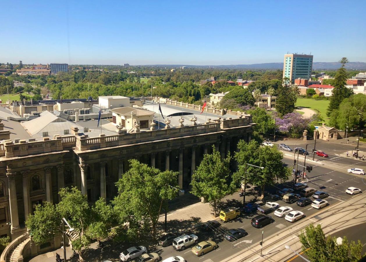 Stamford Plaza Adelaide Hotel Bagian luar foto The photo depicts a cityscape view, showcasing a mix of architectural structures and greenery. In the foreground, there is a large, classical building with columns, suggesting it may be a historical or governmental structure. Surrounding the building